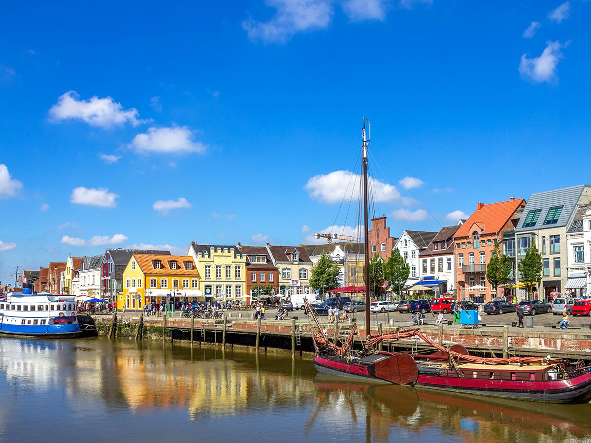 Lebhafte Hafenpromenade mit farbenfrohen Häusern, traditionellen Booten im Wasser und Menschen an einem sonnigen Tag.
