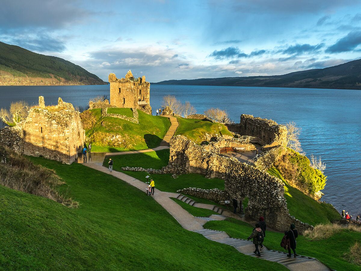 Historische Urquhart Castle Ruinen am Ufer von Loch Ness, Schottland, mit grünen Hügeln und Touristen.