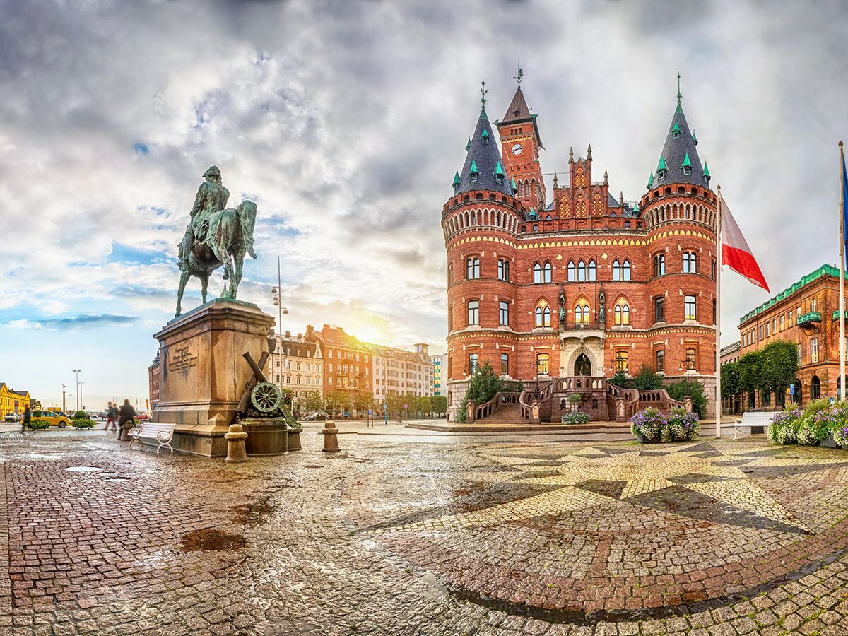 Das historische Rathaus von Helsingborg, ein roter Backsteinbau, und das Reiterdenkmal von Magnus Stenbock auf dem nassen Marktplatz.