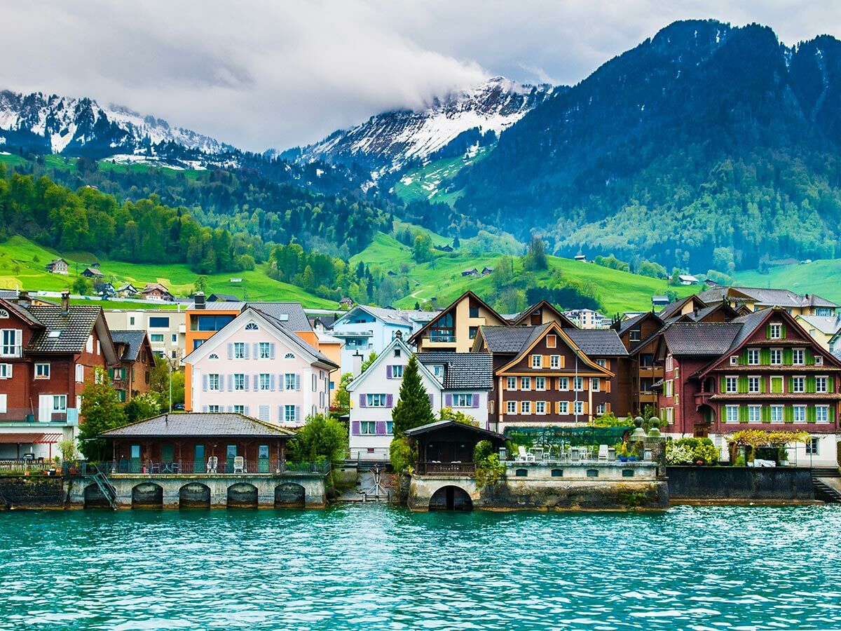Idyllisches Schweizer Dorf mit farbenfrohen Häusern am türkisfarbenen See, umgeben von grünen Hügeln und schneebedeckten Alpen.