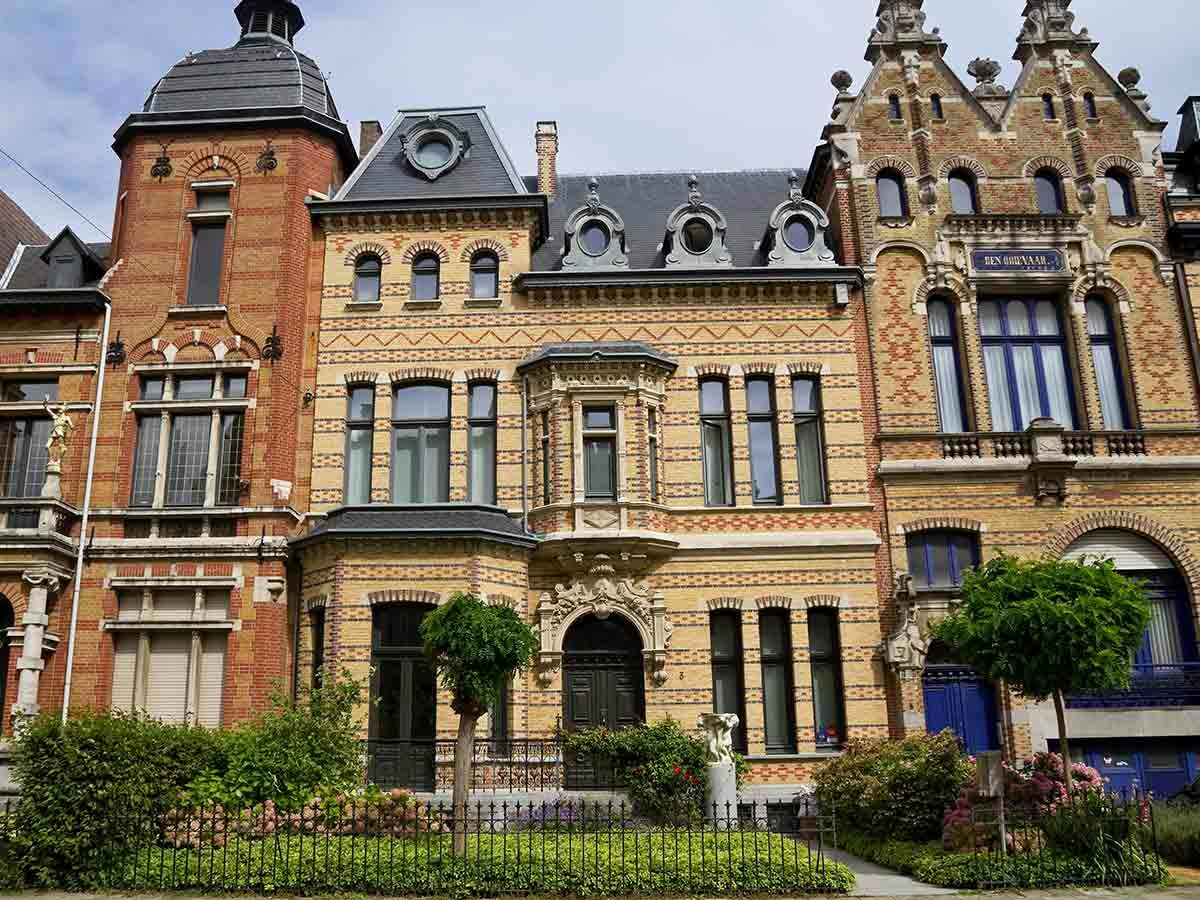 Reihe historischer Stadthäuser mit detailreichen Ziegelfassaden, Türmchen, Giebeln und kunstvollen Verzierungen unter bewölktem Himmel.