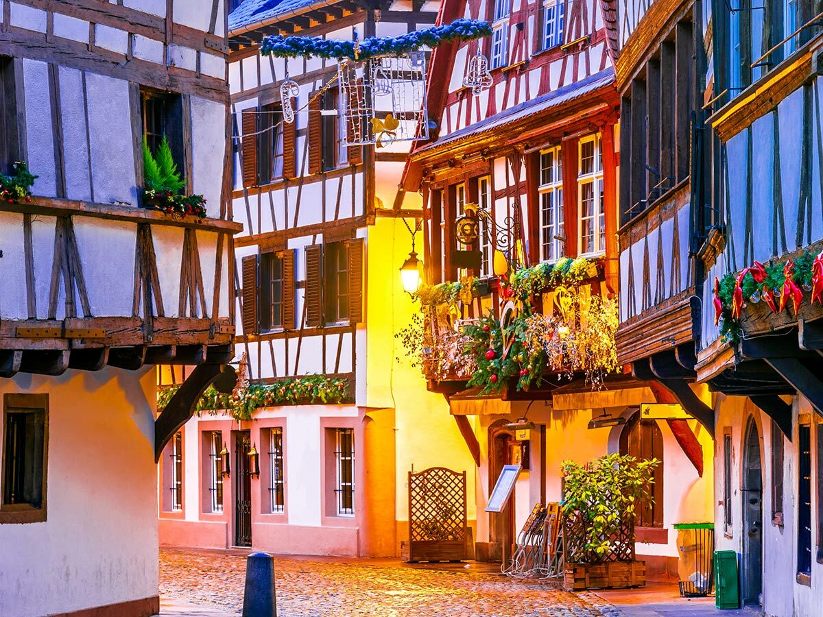Romantische Gasse mit festlich dekorierten Fachwerkhäusern bei Abenddämmerung, erleuchtet von warmen Laternen und Weihnachtsbeleuchtung.