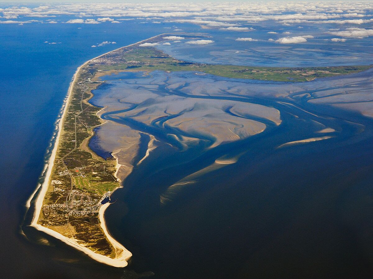 Luftaufnahme der Insel Sylt mit langen Sandstränden, bebauten Gebieten und dem weitläufigen Wattenmeer bei Ebbe.
