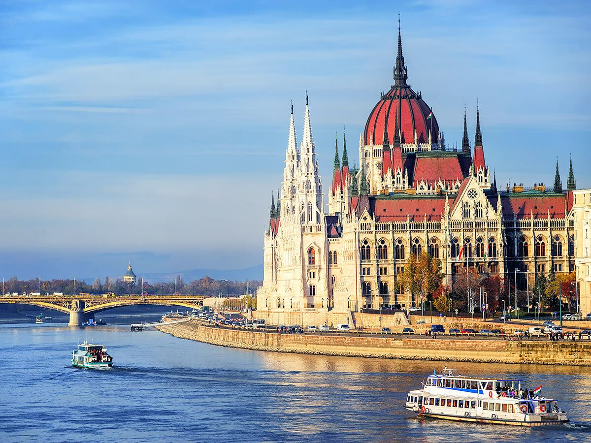 Majestätisches ungarisches Parlamentsgebäude in Budapest am Fluss Donau mit Booten und Brücke unter blauem Himmel.