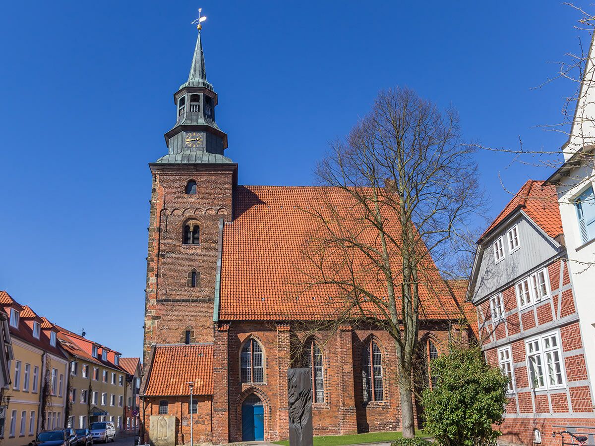 Historische St. Cosmae Kirche in Stade, Norddeutschland, mit Backsteinturm, rotem Dach und Fachwerkhäusern unter blauem Himmel.