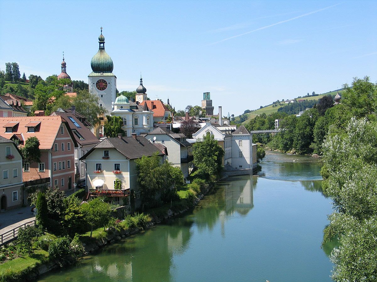 Panoramablick auf die historische Stadt Steyr in Österreich mit dem Fluss Enns, traditionellen Häusern und markanten Kirchtürmen unter blauem Himmel.