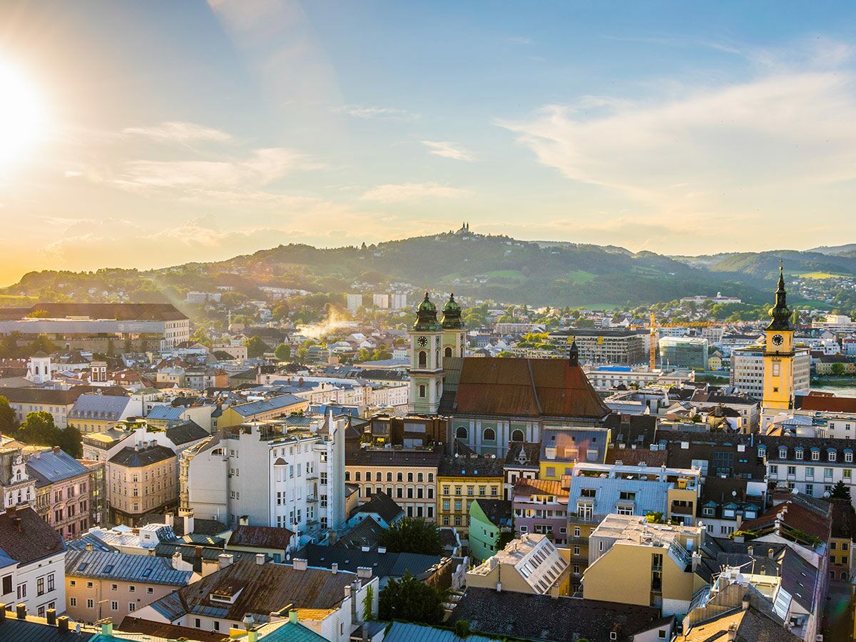 Panoramablick auf Linz, Österreich, bei Sonnenuntergang mit historischen Gebäuden, der Donau und grünen Hügeln im Hintergrund.
