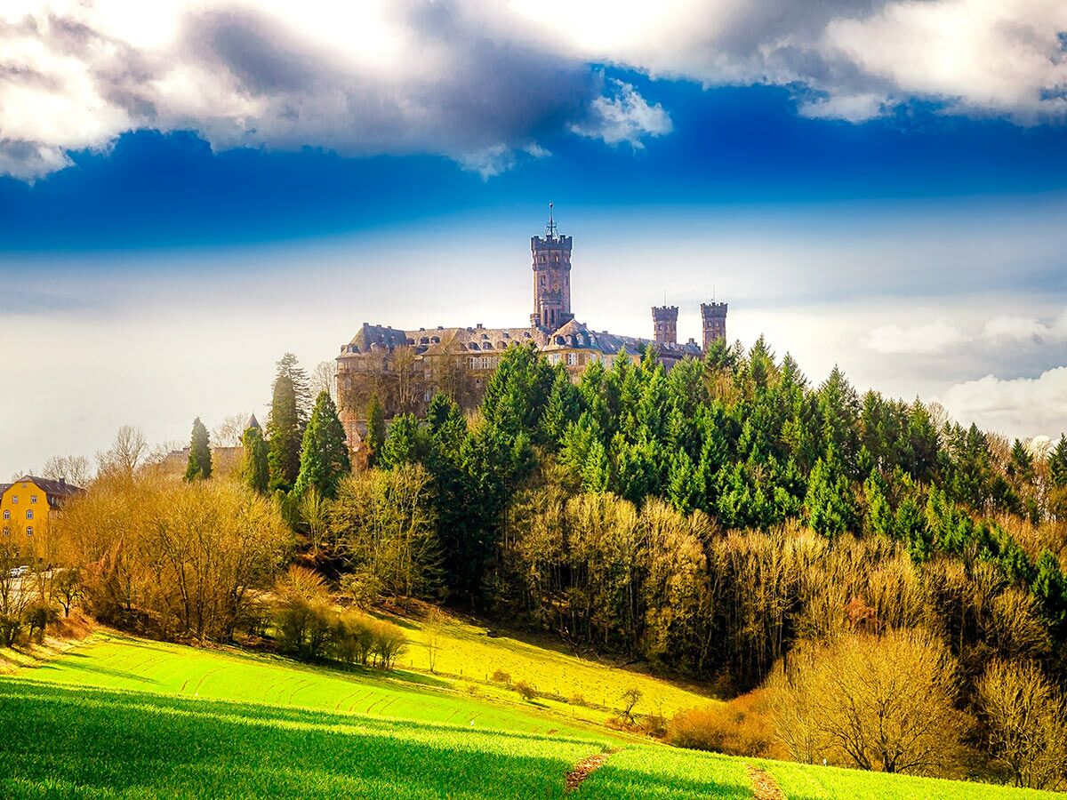 Majestätisches Schloss Braunfels auf bewaldetem Hügel in Hessen, umgeben von grünen Feldern unter blauem Himmel.