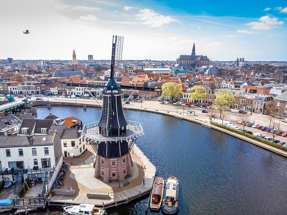 Historische Windmühle De Adriaan in Haarlem am Kanal, umgeben von Häusern und Stadt unter blauem Himmel.