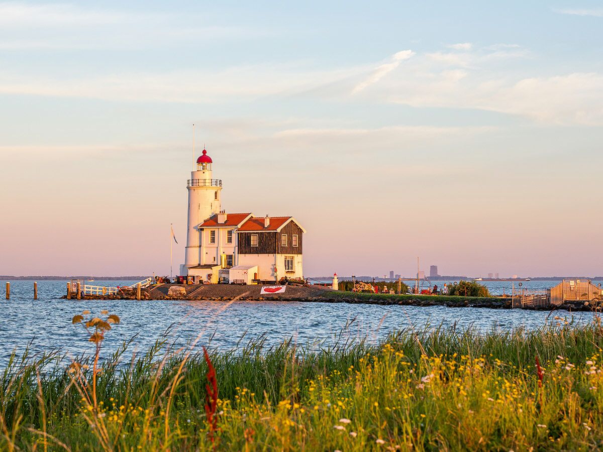 Historischer Leuchtturm Marken am Wasser bei Sonnenuntergang mit Gras und Blumen im Vordergrund.