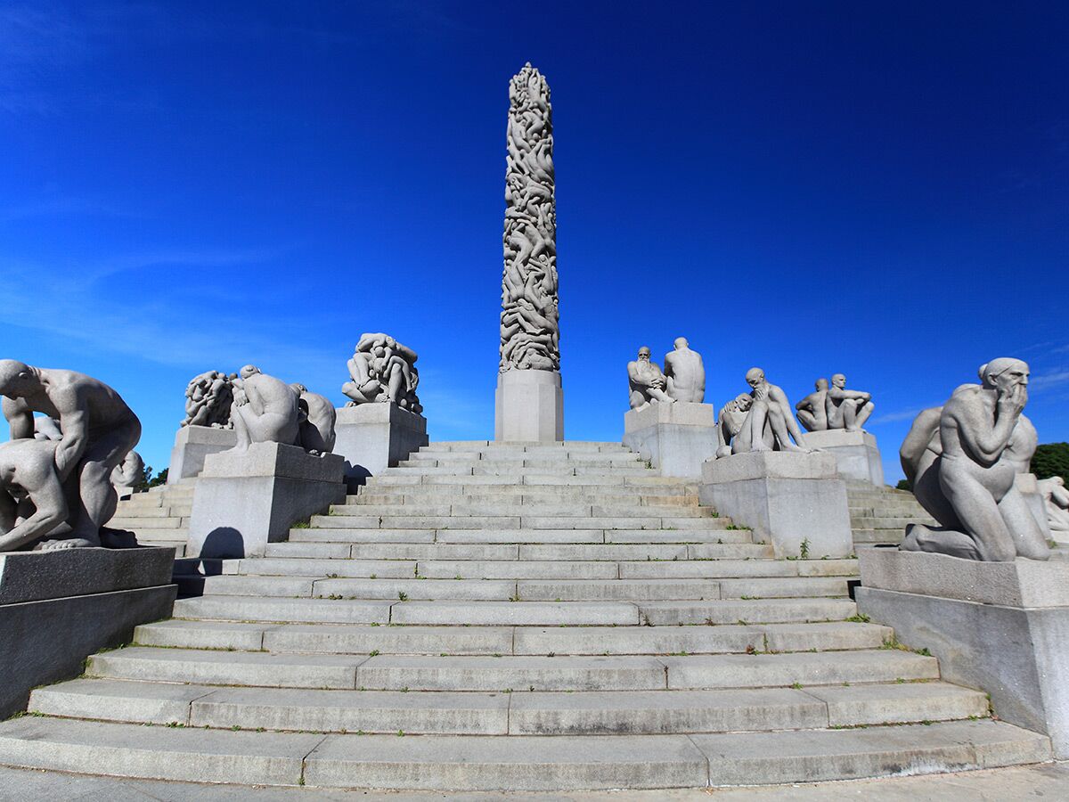 Monumentaler Vigeland-Monolith und zahlreiche menschliche Skulpturen auf einer breiten Steintreppe unter blauem Himmel in Oslo.