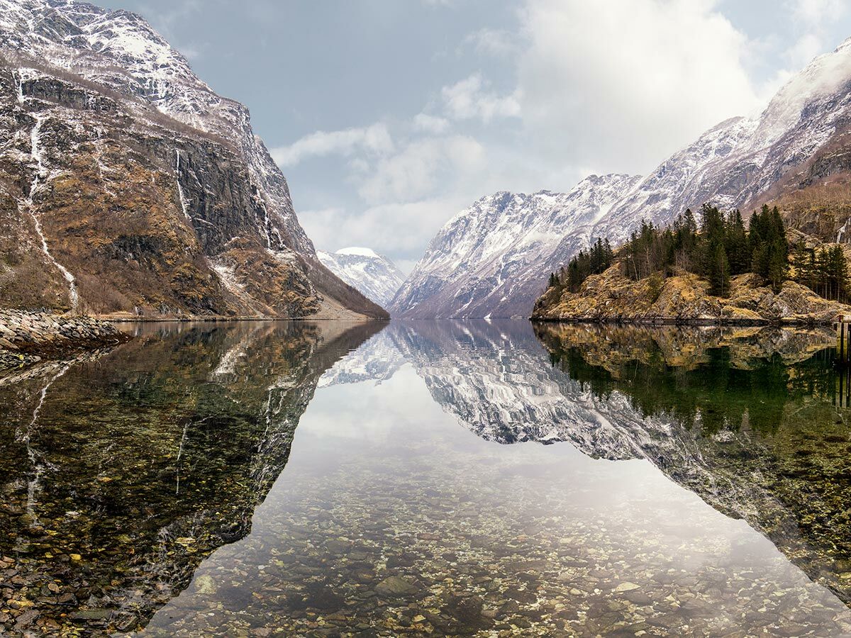 Majestätische norwegische Fjordlandschaft mit schneebedeckten Bergen, klarem Wasser, felsiger Küste und perfekter Spiegelung.