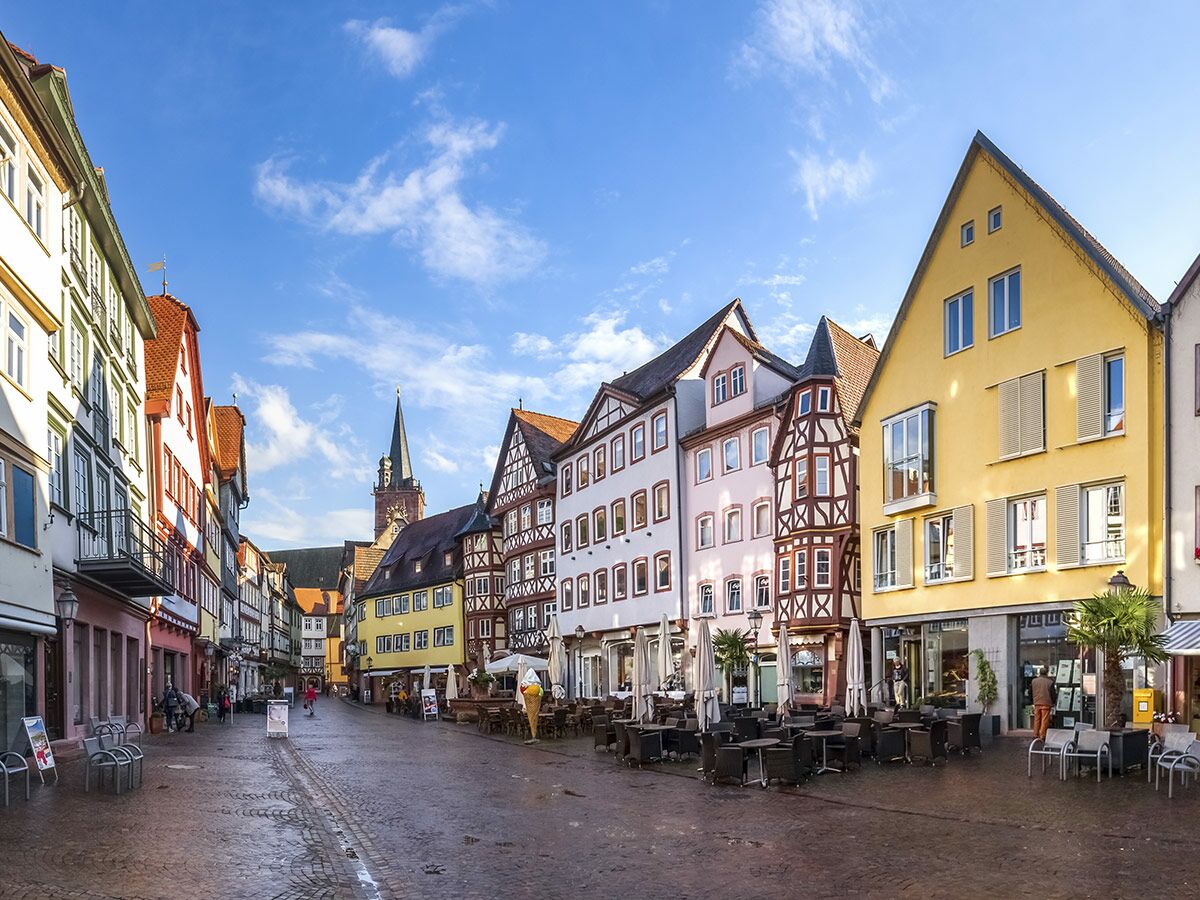 Malerische Altstadtstraße mit bunten Fachwerkhäusern, Straßencafés und Kirchturm unter blauem Himmel in Deutschland.