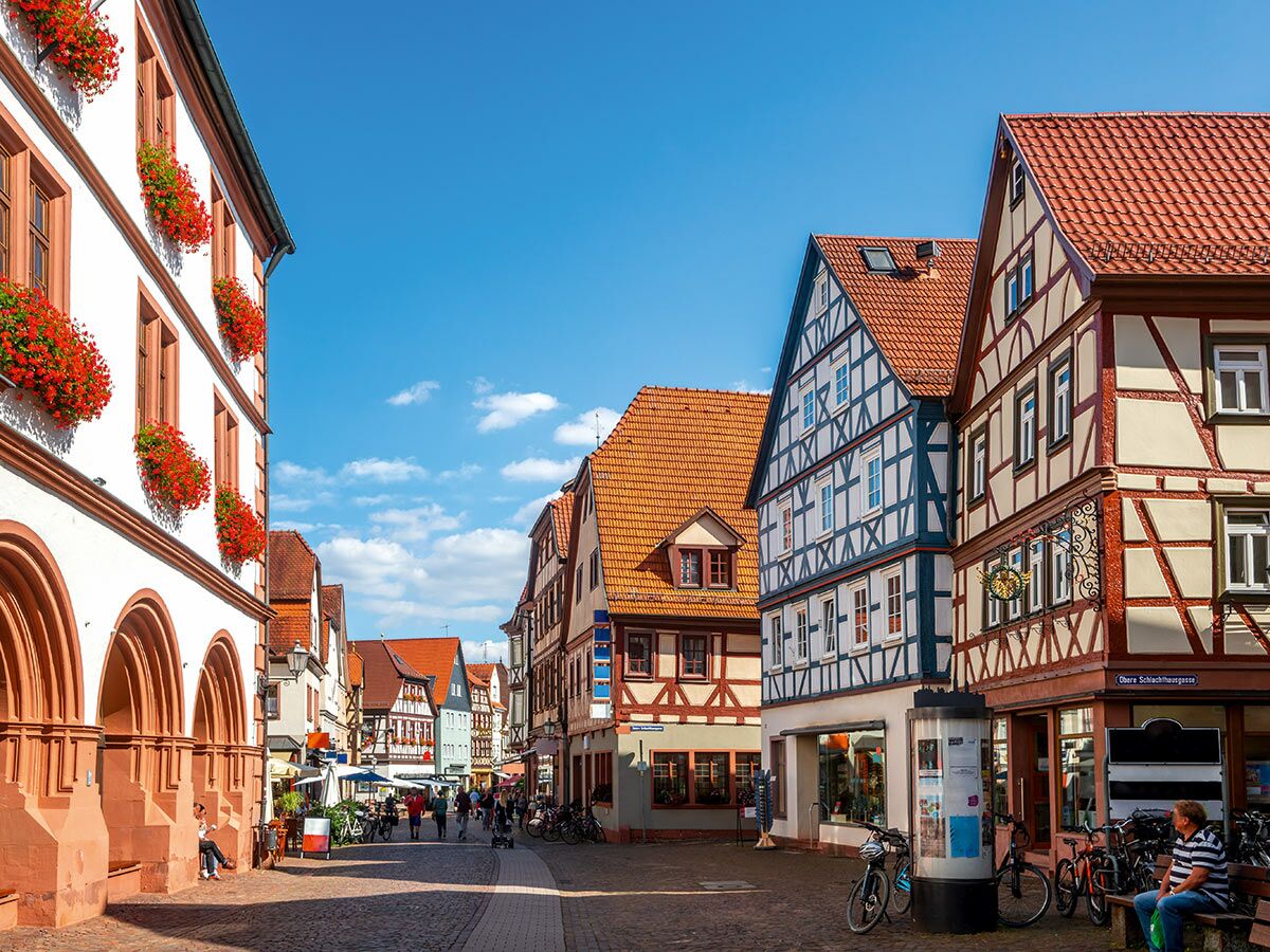 Blick auf die historische Altstadt von Gelnhausen mit bunten Fachwerkhäusern, belebter Fußgängerzone und blauem Himmel.