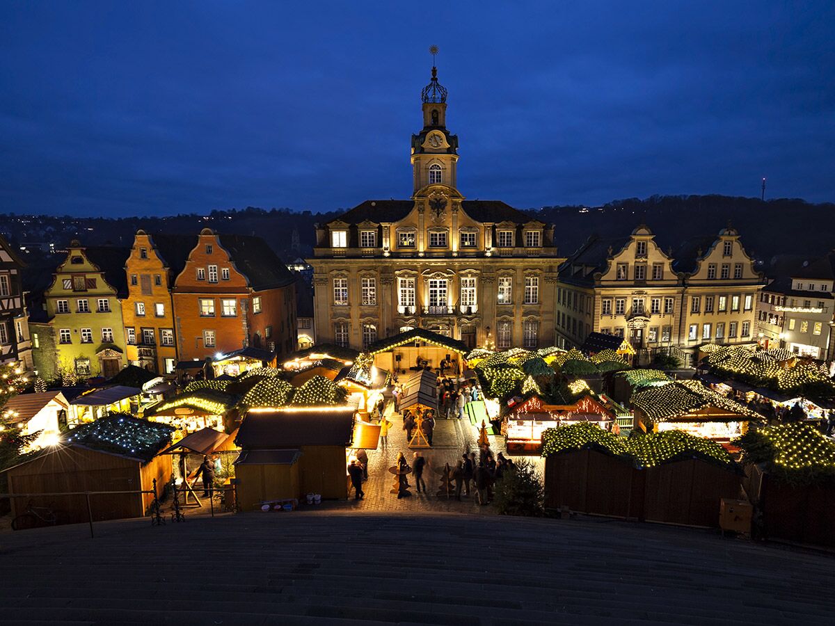 Festlicher Weihnachtsmarkt in Tübingen bei Einbruch der Dunkelheit, beleuchtete Stände vor historischen Gebäuden.