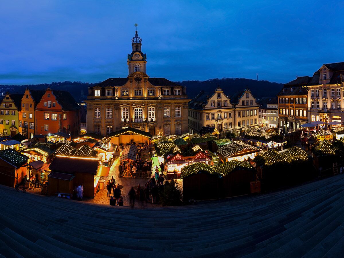 Festlicher Weihnachtsmarkt bei Nacht auf einem historischen Marktplatz in einer deutschen Stadt, mit beleuchteten Ständen und Gebäuden.