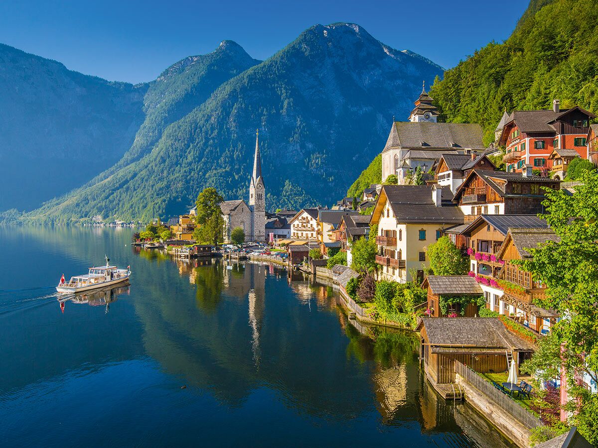 Malerisches Dorf Hallstatt am Hallstätter See, Österreich, mit Kirche, Häusern, Bergen und Boot auf ruhigem Wasser.