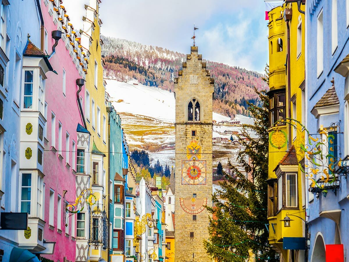 Malerische Alpenstadt mit bunten historischen Häusern, Gasse, Uhrturm und schneebedeckten Bergen im Winter.