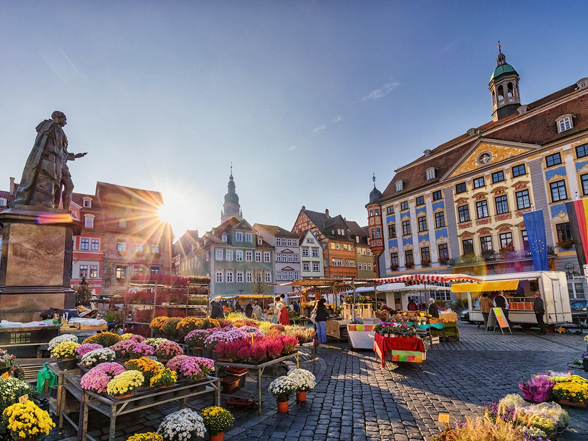Blumenmarkt Gotha Marktplatz. Sonnenbeschienener historischer Platz mit Ständen, bunten Blumen, Menschen und Statue Herzog Ernst.