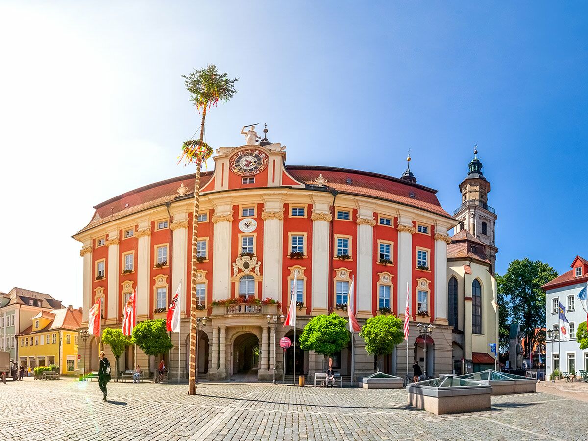 Historisches Rathaus Schongau am Marktplatz mit Maibaum, Kirchturm und traditionellen Gebäuden unter blauem Himmel.