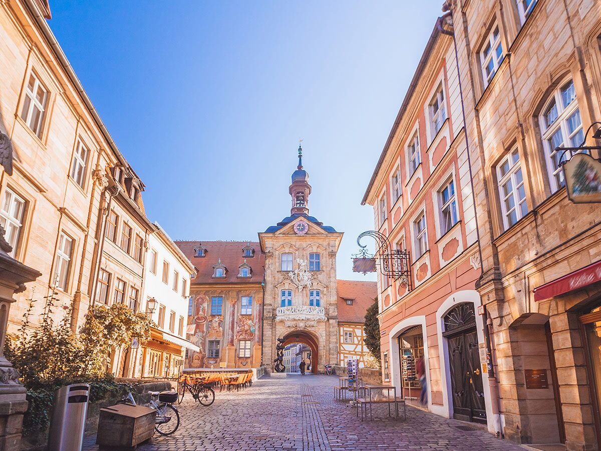 Altes Rathaus Bamberg, Deutschland. Historische Gasse mit Gebäuden, Kopfsteinpflaster, Fahrrädern und klarem blauen Himmel.