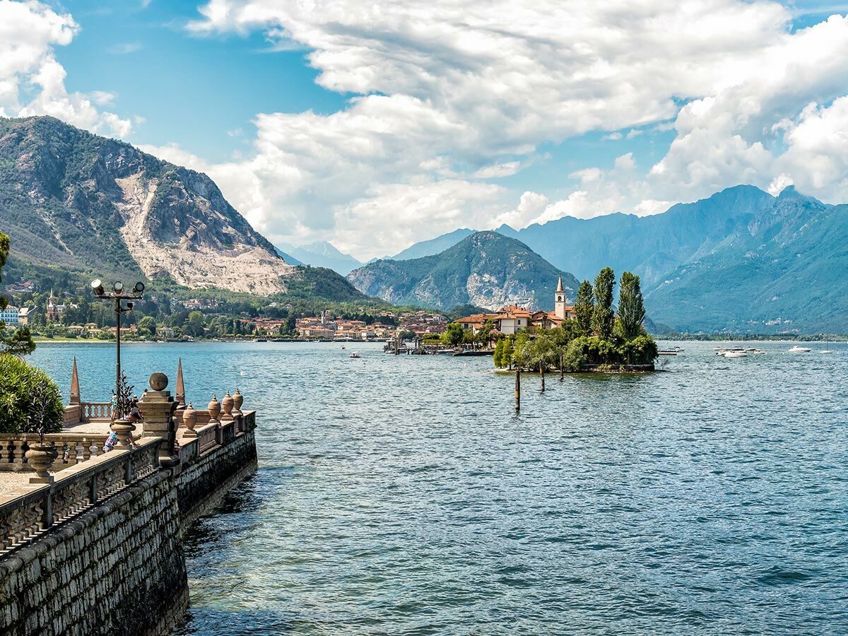 Malerische Landschaft des Lago Maggiore mit Isola dei Pescatori, Bergen und historischer Promenade im Vordergrund.