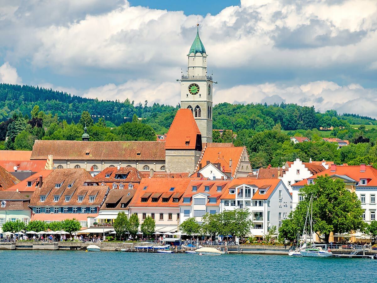 Malerische Ansicht der Altstadt von Lindau am Bodensee mit Kirche, roten Dächern und belebter Uferpromenade.