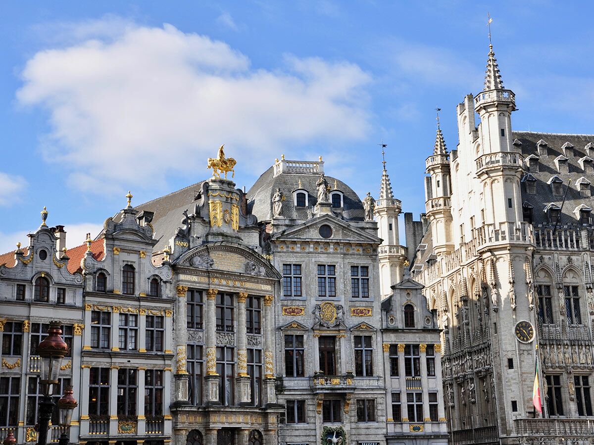 Ornate Gildehäuser und historische Bauten am Grand-Place in Brüssel unter blauem Himmel mit Wolken, goldene Akzente.
