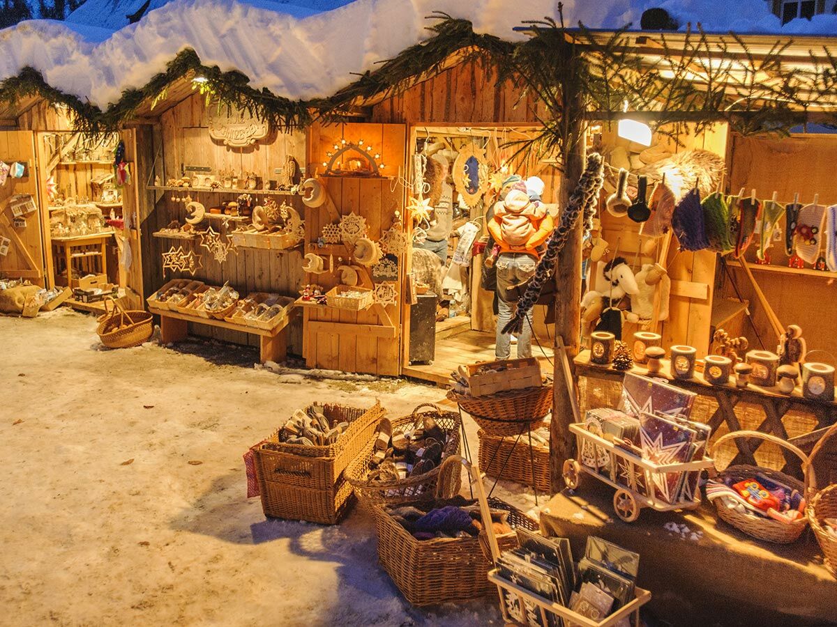 Ein festlicher Weihnachtsmarkt bei Nacht mit beleuchteten Holzständen, die handgefertigte Dekorationen und Geschenke verkaufen, bedeckt mit Schnee.