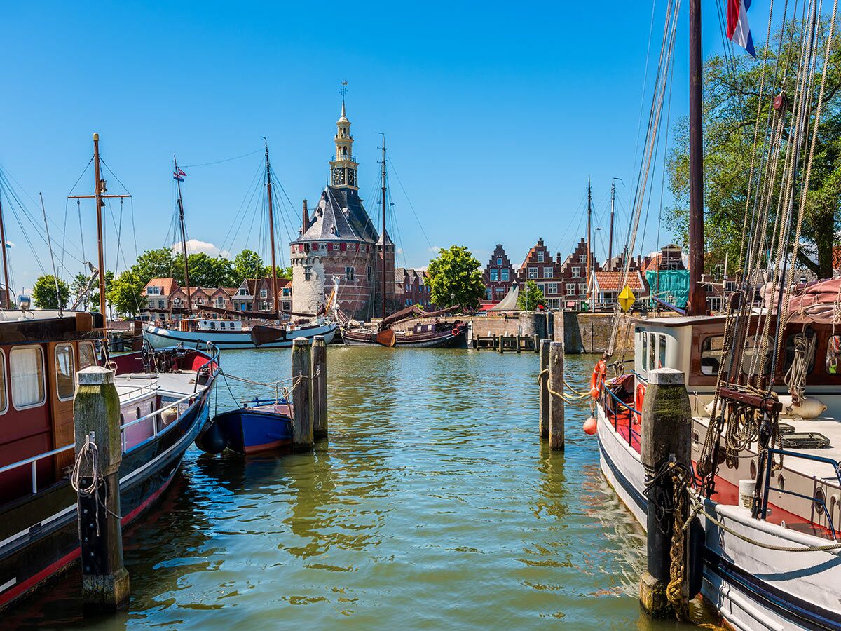 Historischer Hafen Enkhuizen, Niederlande, mit traditionellen Segelbooten, Giebelhäusern und dem Drommedaris-Turm unter blauem Himmel.