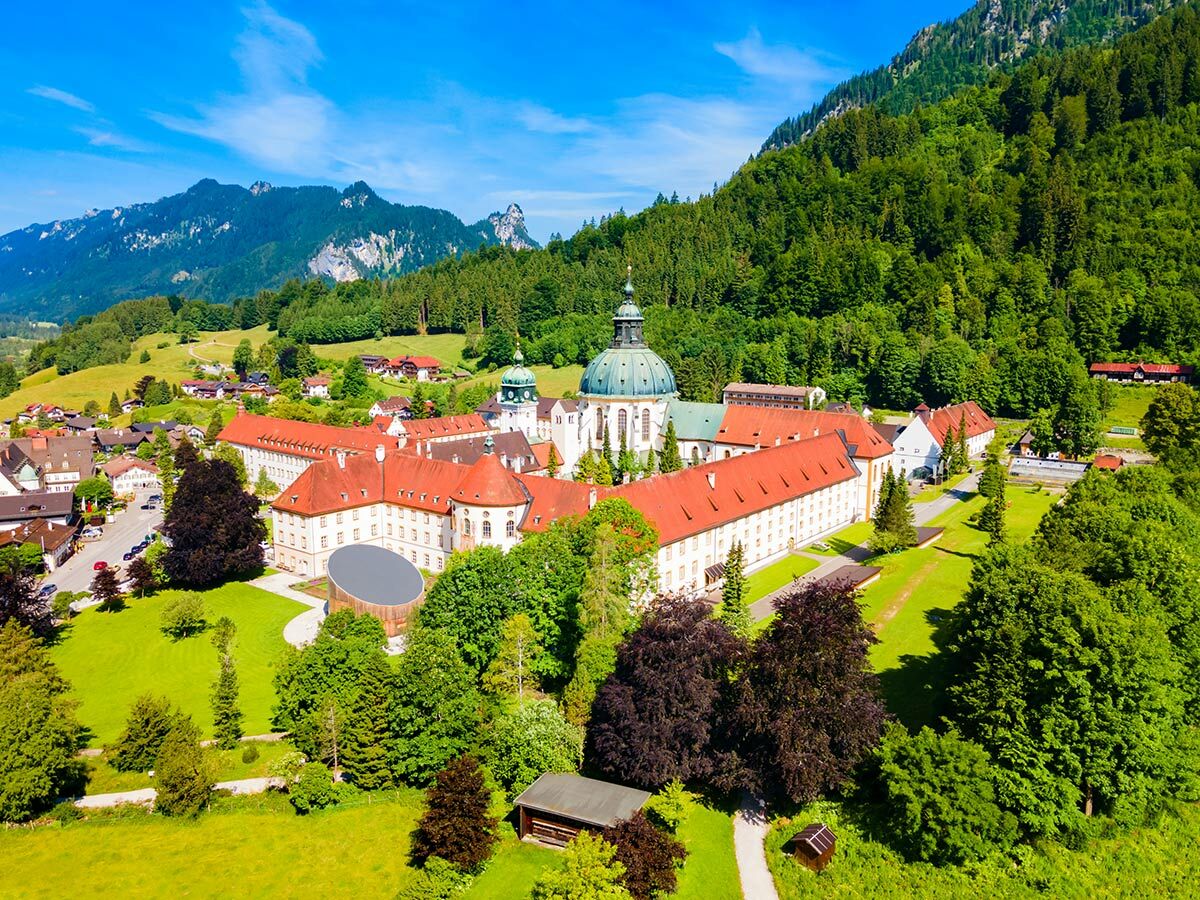 Luftaufnahme von Kloster Ettal in Bayern mit grünen Bergen und Wäldern unter blauem Himmel im Sommer.