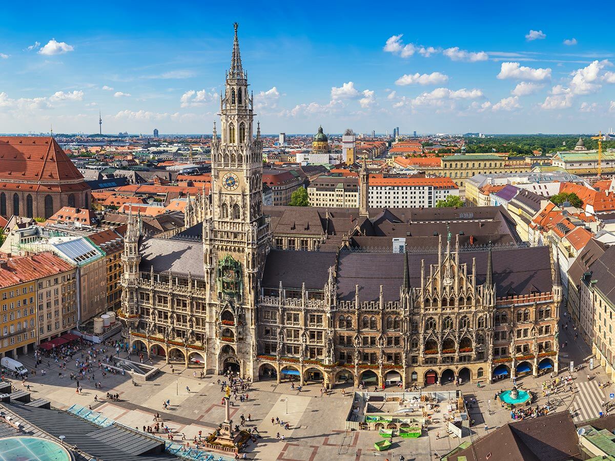 Panoramablick auf Münchens Marienplatz mit dem Neuen Rathaus, belebtem Platz und Stadtkulisse unter blauem Himmel.