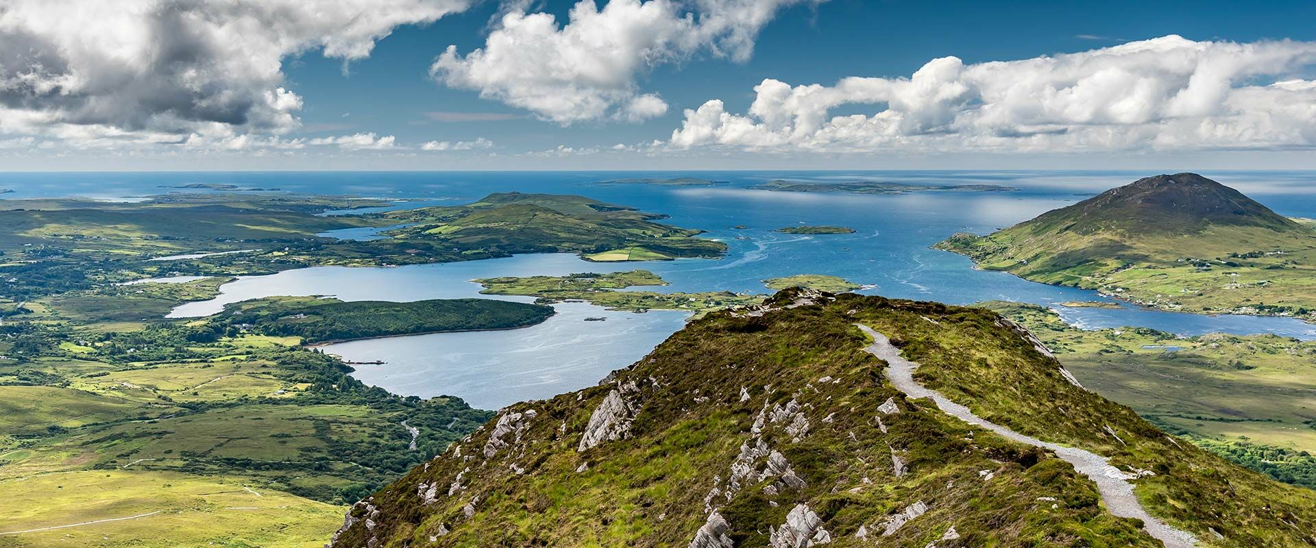 Atemberaubende Panoramaansicht von Irlands grünen Hügeln und Seen, die auf den Ozean treffen, mit Wanderweg.