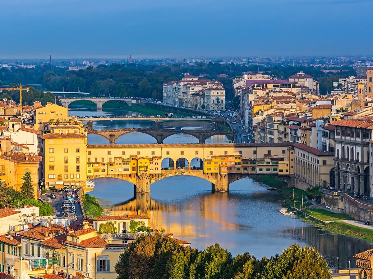 Panoramablick auf Florenz mit dem Arno, der historischen Ponte Vecchio und den umliegenden Gebäuden in warmem Licht.