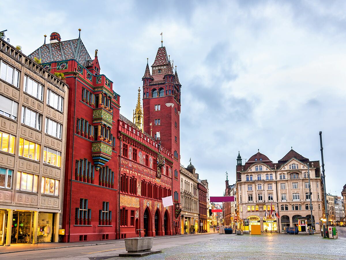 Historisches Rathaus Basel mit roter Fassade, beleuchteten Fenstern und Kopfsteinpflasterstraße bei Dämmerung in der Schweiz.