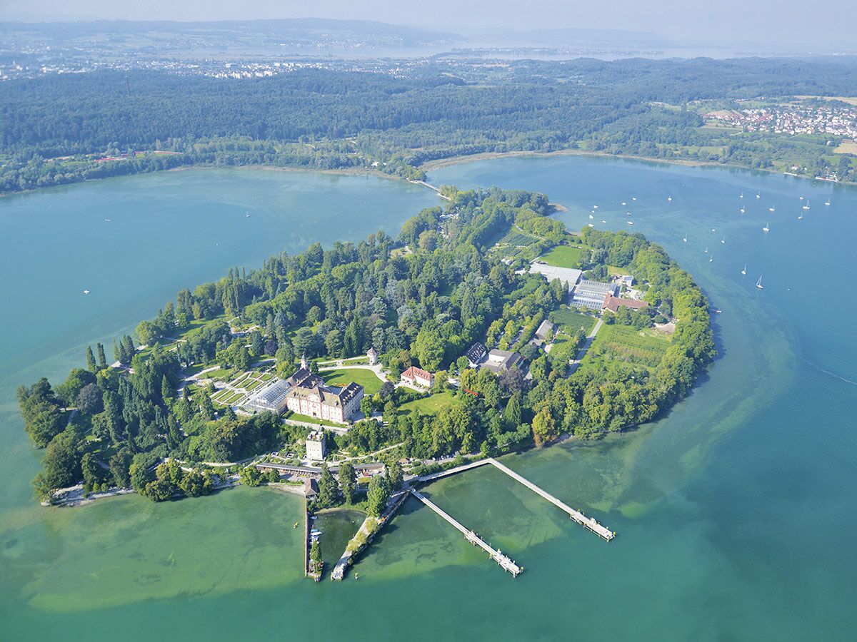 Luftaufnahme der Blumeninsel Mainau im Bodensee mit Schloss, Gärten, Gewächshäusern und Bootsanlegern.