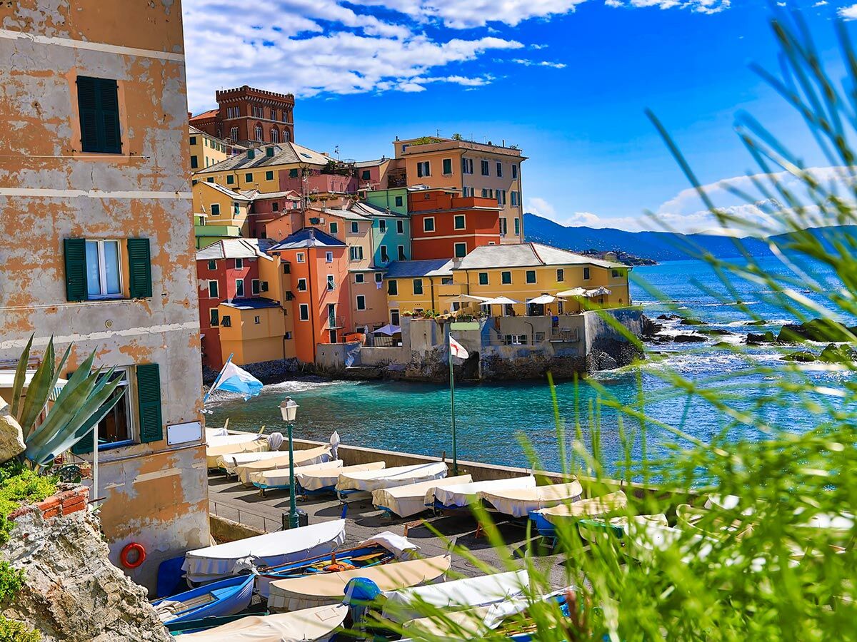 Blick auf das malerische Fischerdorf Boccadasse in Genua, Italien, mit bunten Häusern, Booten im Hafen und türkisblauem Meer.