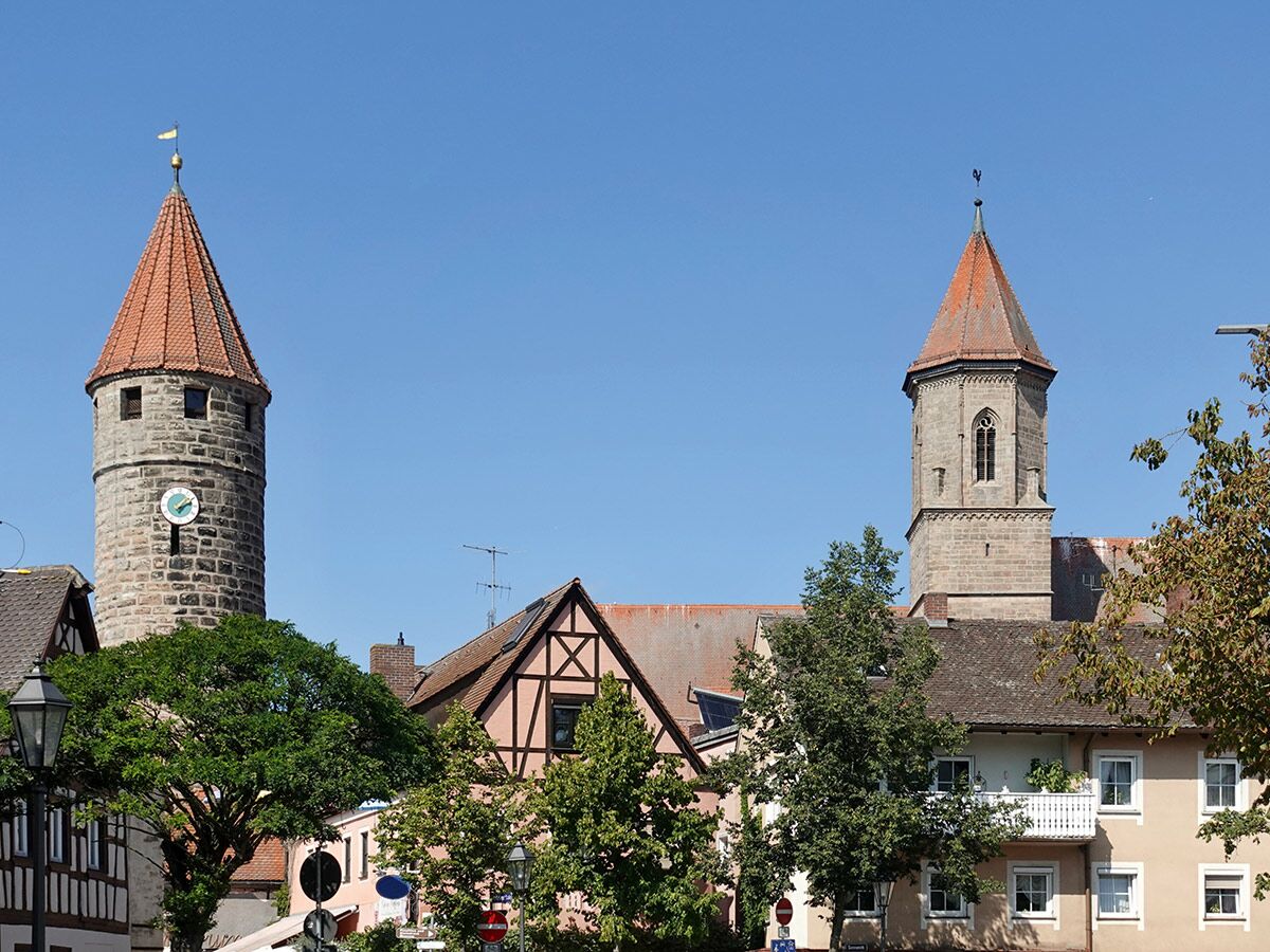 Zwei historische Steintürme mit roten Dächern und einer Uhr über den Dächern einer deutschen Altstadt bei blauem Himmel.