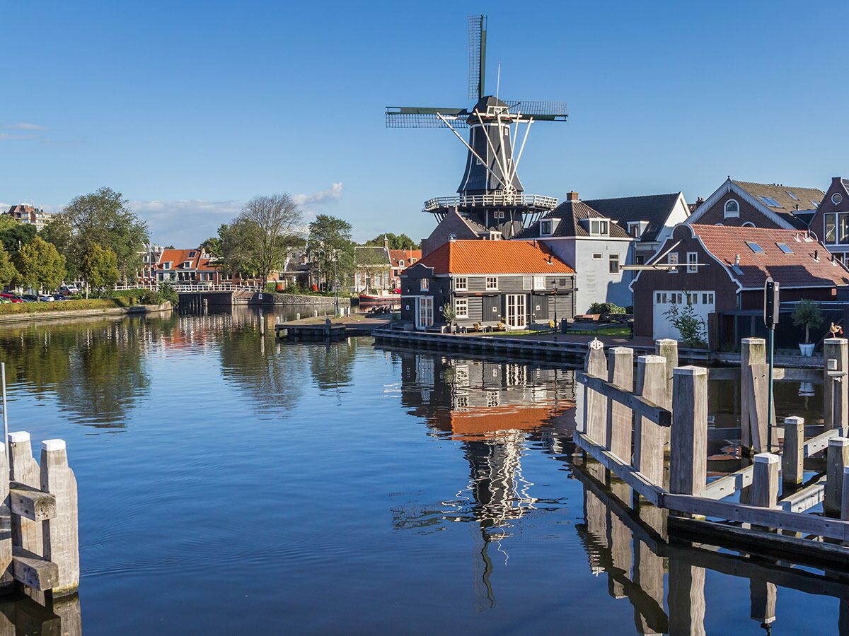 Historische Windmühle De Adriaan und bunte Häuser am Fluss Spaarne in Haarlem unter blauem Himmel.