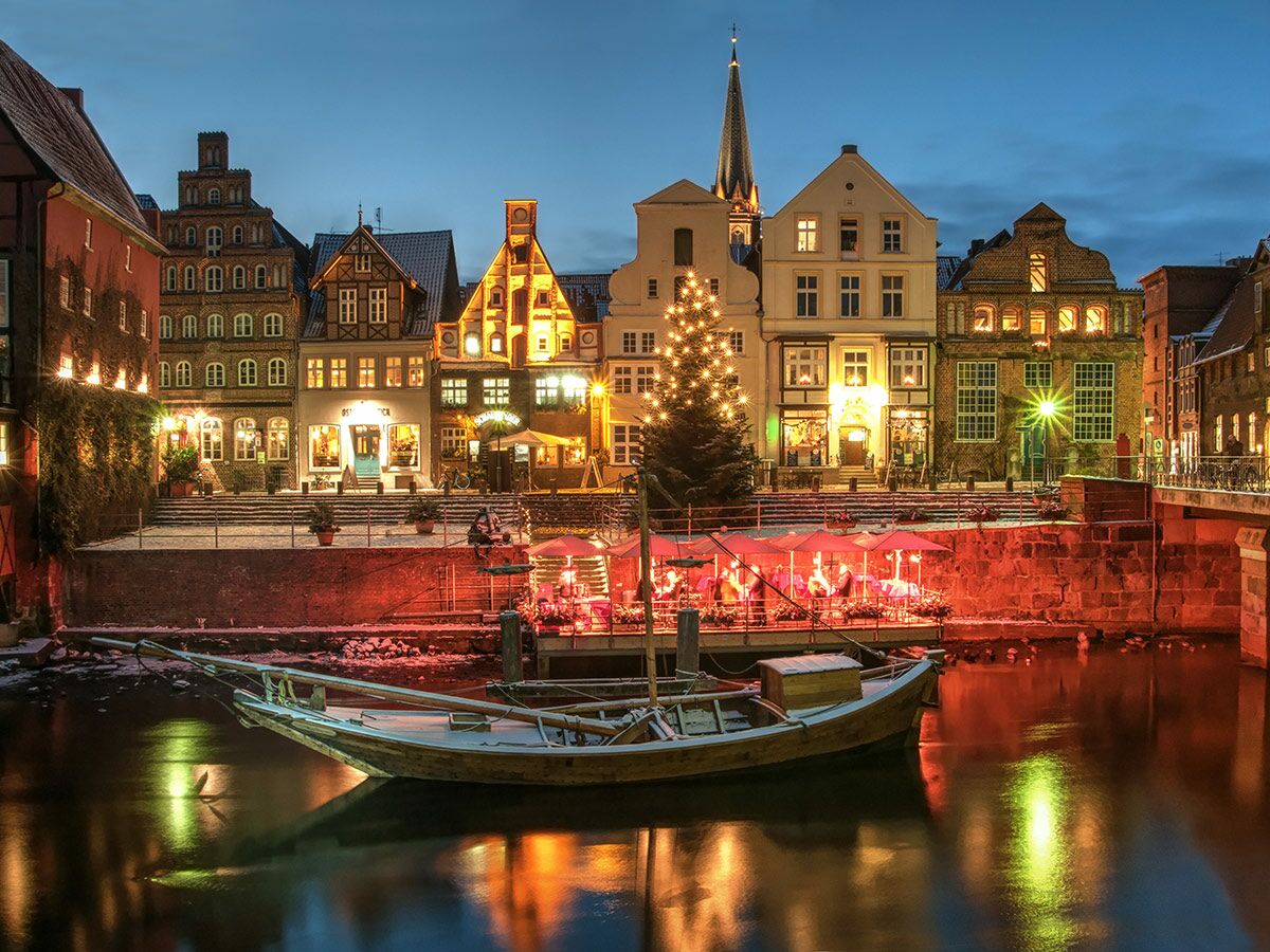 Historische Lüneburg Winteransicht mit festlich beleuchteten Giebelhäusern, Weihnachtsbaum und Boot im Kanal bei Nacht.