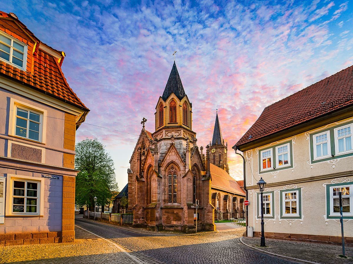 Malerische deutsche Altstadt mit historischer Kirche, Kopfsteinpflasterstraße und farbenprächtigem Sonnenuntergangshimmel.