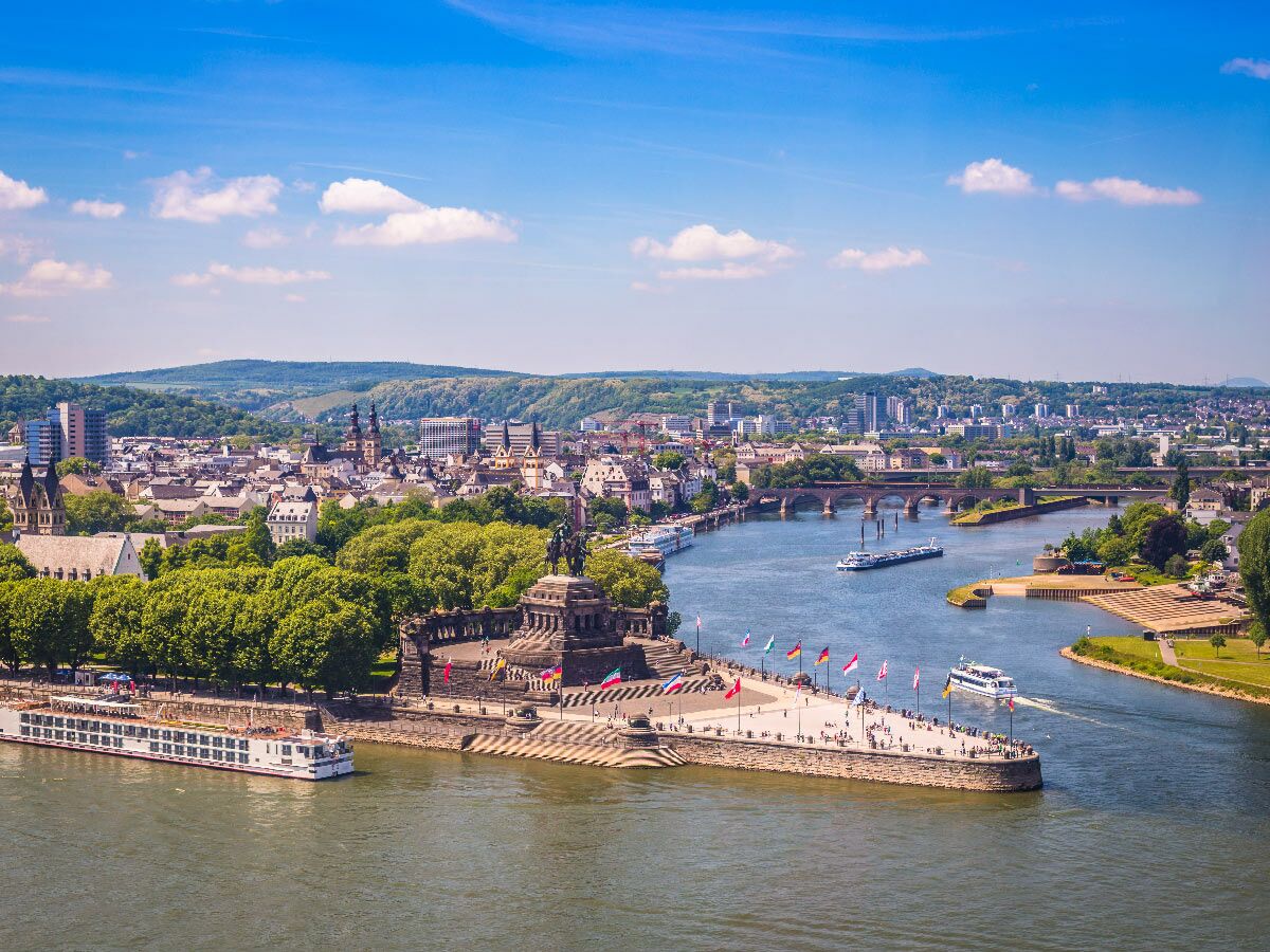 Luftaufnahme Koblenz: Deutsches Eck, Zusammenfluss Rhein-Mosel, Stadt, Schiffe, grünen Hügeln, blauer Himmel.