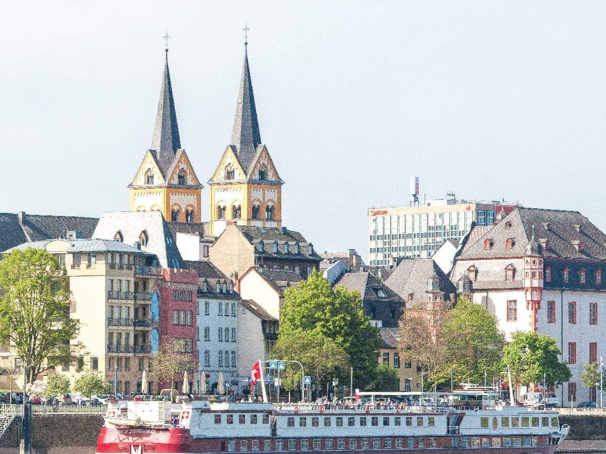 Panoramablick auf das Kölner Rheinufer mit der Groß St. Martin Kirche, historischen Gebäuden und einem Flusskreuzfahrtschiff.
