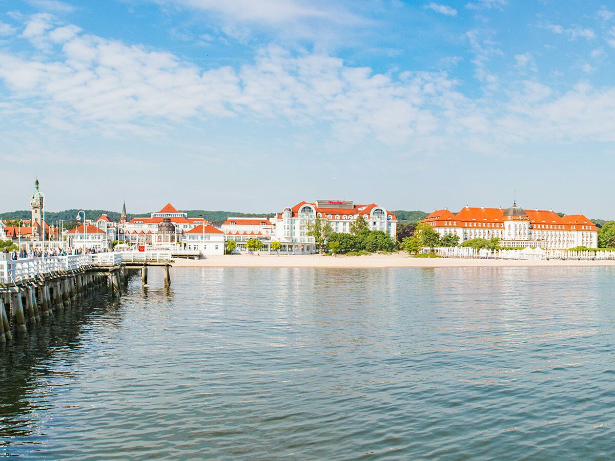 Ansicht des Sopot Piers mit Menschen, weißen Strandhotels mit roten Dächern und dem Strand an der Ostsee.