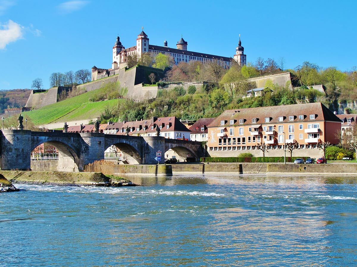 Blick auf die Festung Marienberg über Weinbergen, die Alte Mainbrücke und historische Gebäude am Fluss Main in Würzburg.