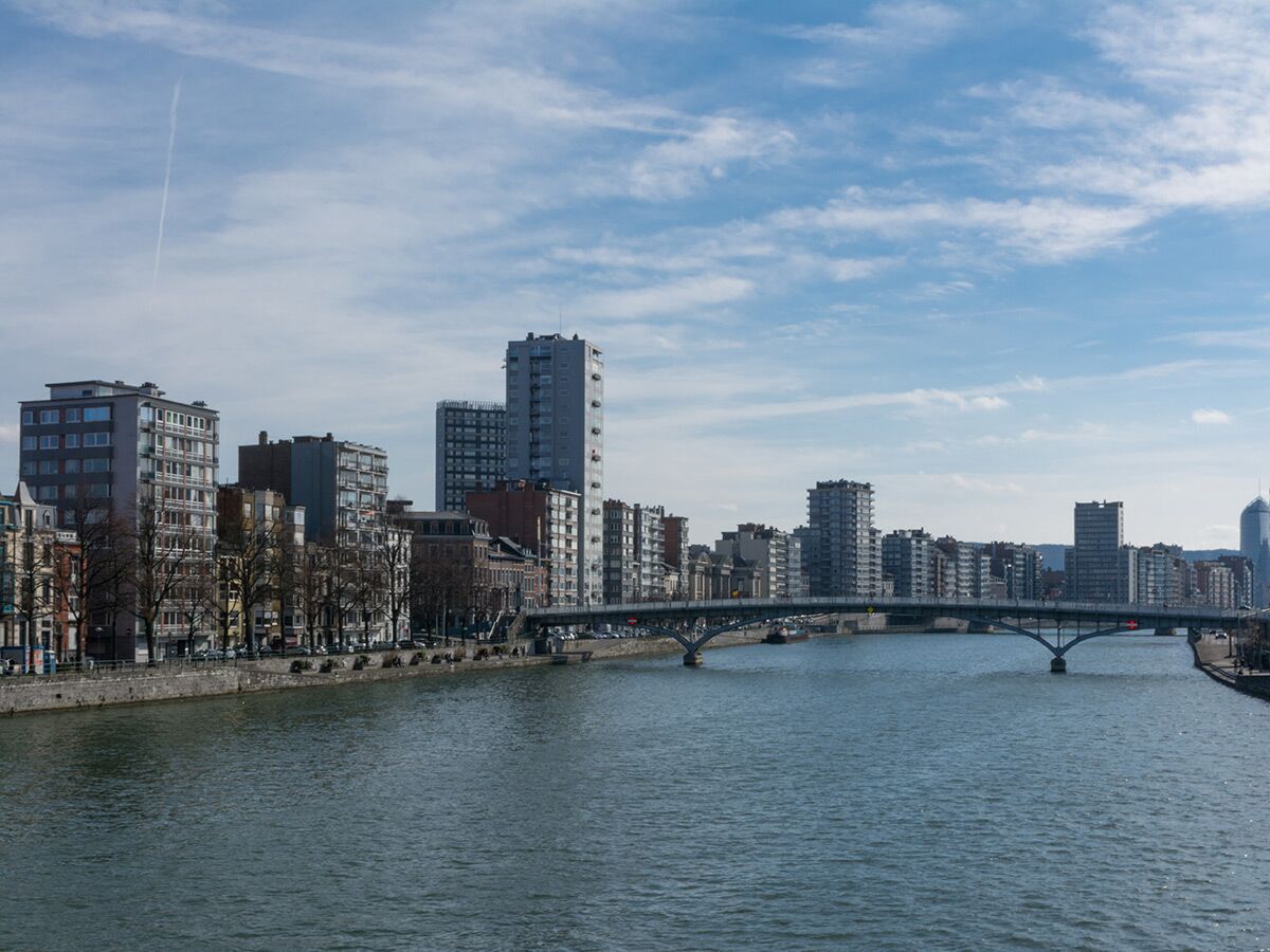Stadtansicht von Lüttich mit der Maas, einer Brücke und der Skyline moderner und traditioneller Gebäude unter blauem Himmel.
