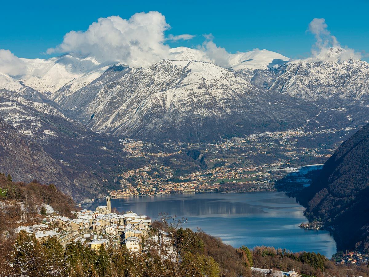 Majestätische Winterlandschaft mit schneebedeckten Alpen, blauem Bergsee und einem malerischen Dorf am Hang unter klarem Himmel.