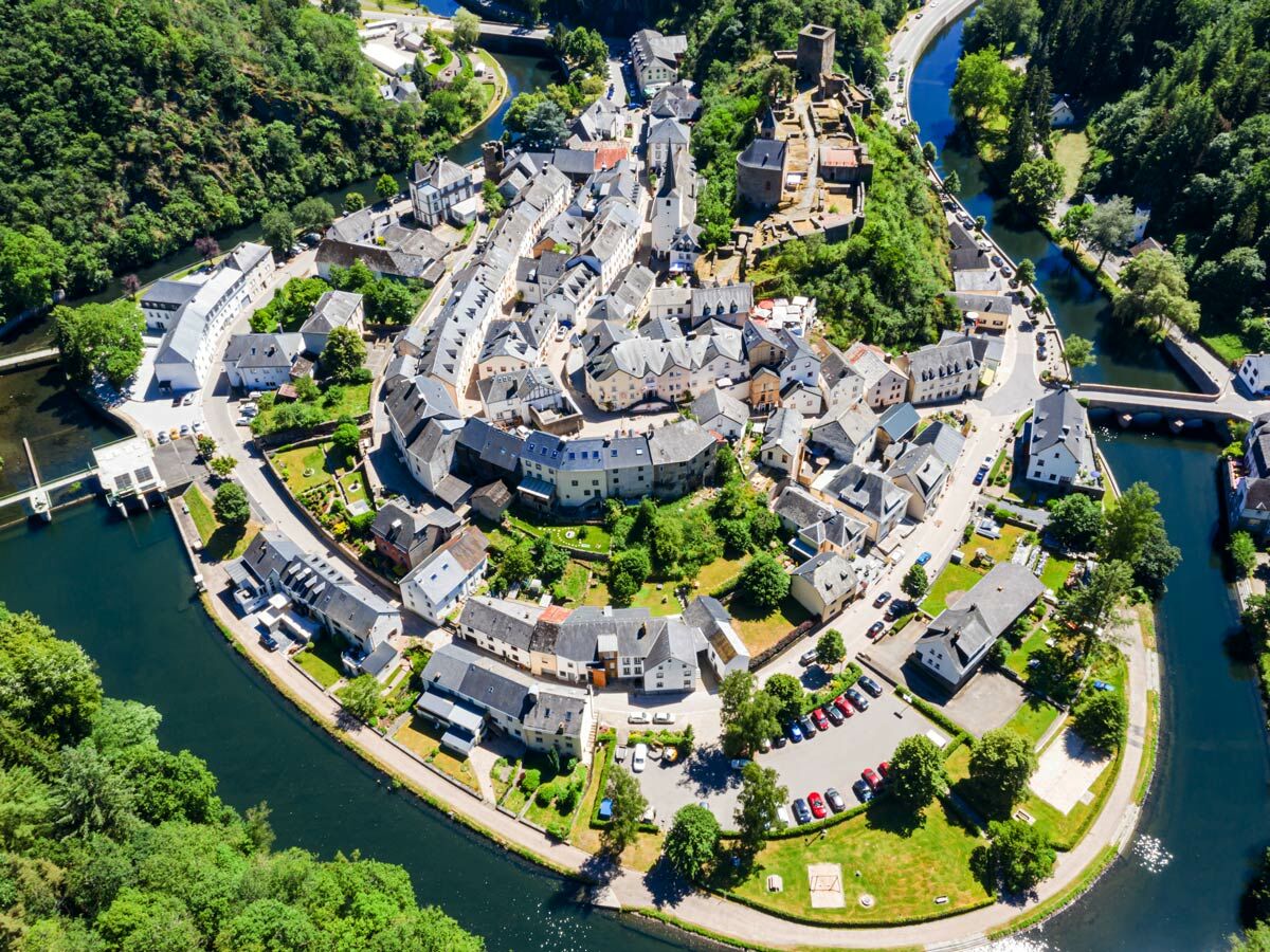 Luftaufnahme: malerische Stadt am Fluss in einem grünen Tal mit historischer Architektur, Burgruine, Kirche und Brücken.