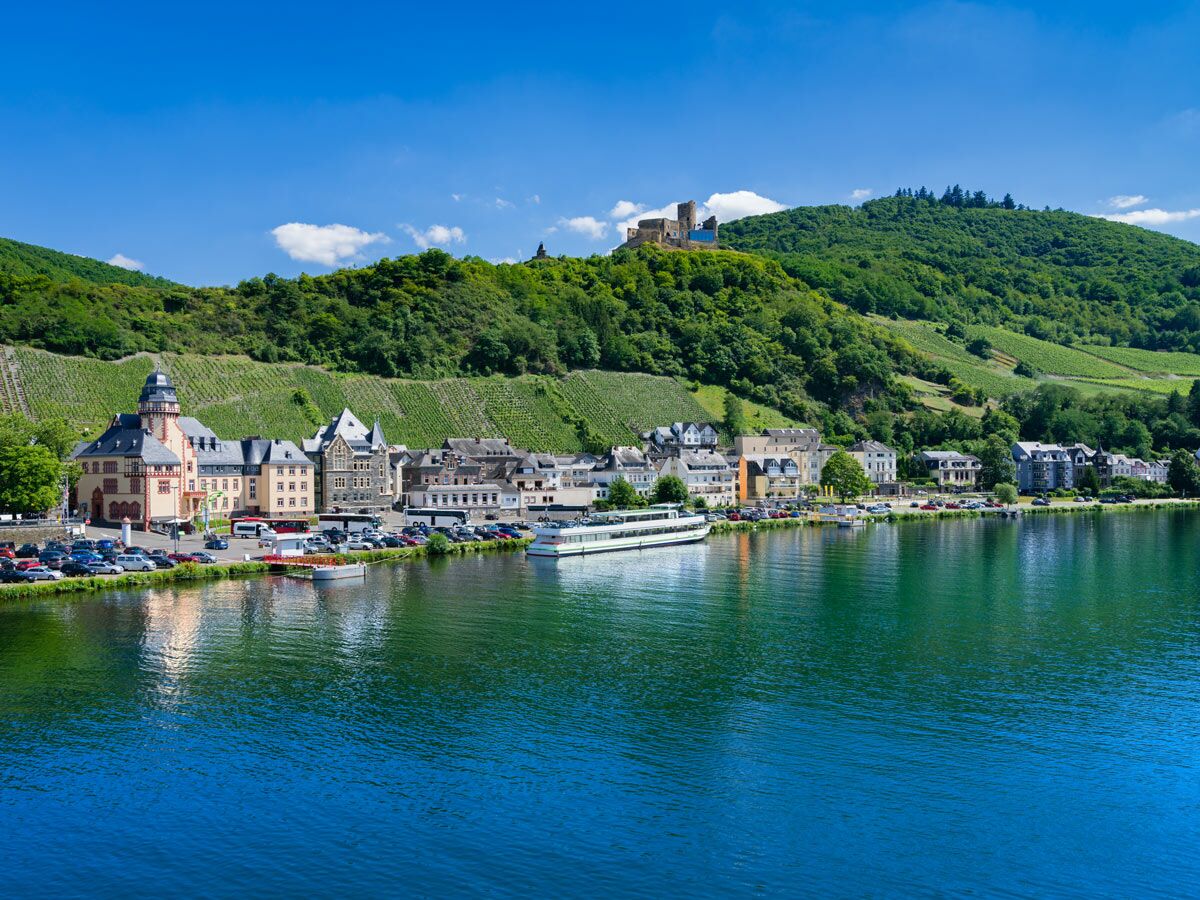 Panoramablick auf Bernkastel-Kues an der Mosel mit Burg Landshut, Weinbergen und historischen Gebäuden unter blauem Himmel.