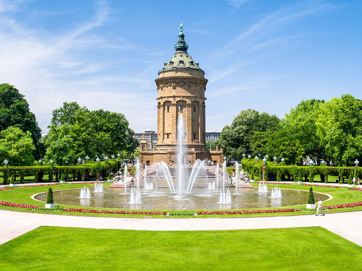 Der Wasserturm Mannheim im Friedrichsplatz Park mit großer Brunnenanlage, grünen Bäumen und blauem Himmel an einem sonnigen Tag.